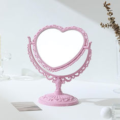 a pink heart shaped mirror sitting on top of a table next to a vase with flowers