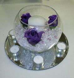 a glass vase with purple flowers and candles on it sitting on a silver platter