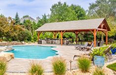 a backyard with a pool and gazebo surrounded by trees, shrubs and rocks in the foreground