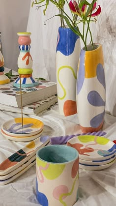 colorful vases with flowers in them sitting on a table next to plates and magazines