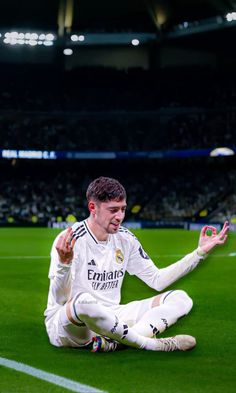 a man sitting on the ground in front of a soccer field with his hands up