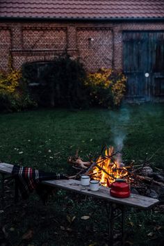 a campfire in the middle of a yard next to a building and picnic table