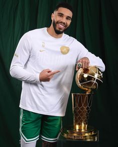 a man in green shorts and white shirt holding up a basketball ball next to a trophy