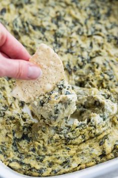 a hand dipping a cracker into a bowl of spinach dip