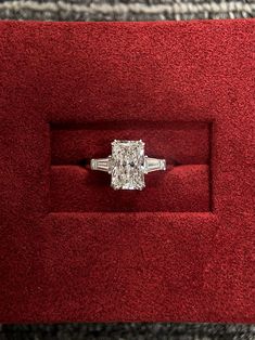 an engagement ring in a red velvet box with a diamond center stone on the band