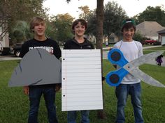 two boys holding up paper and scissors in front of a tree with a notepad attached to it