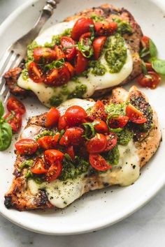 two pieces of chicken covered in pesto and cherry tomatoes on a white plate with a fork