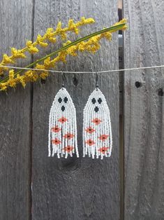 two beaded ghost earrings hanging on a clothes line with yellow flowers in the background