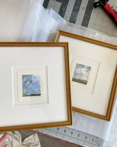 two framed pictures sitting on top of a table next to a pair of scissors and tape