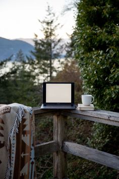 a laptop computer sitting on top of a wooden table next to a cup and saucer