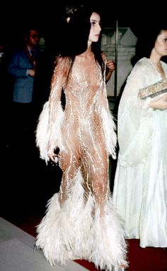 a woman in a white feathered dress is walking down the street with other people behind her