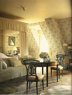 a living room filled with furniture and walls covered in floral wallpaper, next to a bed