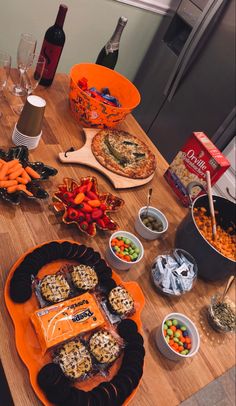 a wooden table topped with plates and bowls filled with food next to bottles of wine