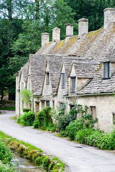 an old stone house with ivy growing on it's roof and windows next to a stream