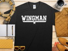 Elevate your wardrobe with this Wingman T-Shirt featuring a retro graphic design. Perfect for those who love to play the role of a supportive wingman, this funny tee is an excellent gift for friends or family members. The cool wingman design adds a touch of character to your casual outfits, making it a standout piece in your apparel collection.  The Gildan 5000 t-shirt features a medium-weight 100% cotton fabric with no side seams for a seamless fit. Enjoy the classic fit and family sizing optio Wingman Gifts, Retro Graphic Design, Navy Veteran, Design Cool, Design Graphique, Us Navy, Environmental Impact, Comfort Style, Funny Tees