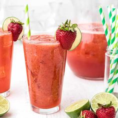 three glasses filled with strawberry limeade and two strawberries next to limes on the table