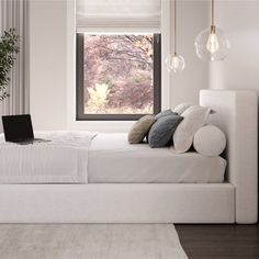 a white bed sitting under a window next to a laptop computer