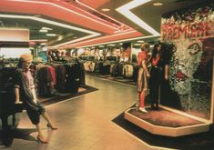 two women are standing in the middle of a shopping mall with clothes on display behind them