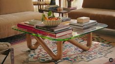 a glass table topped with books and a bowl of fruit on top of it next to a couch