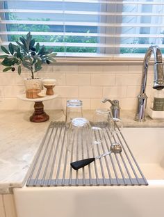 a kitchen sink filled with dishes and utensils next to a window covered in blinds