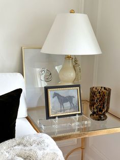 a glass table topped with a lamp next to a white chair and a framed photo