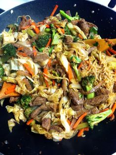 stir fry with beef, noodles and vegetables in a black bowl on a table top