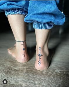 two people with tattoos on their feet standing in front of a wooden floor and wearing blue pants