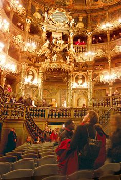 people are standing in an ornate theatre with chandeliers