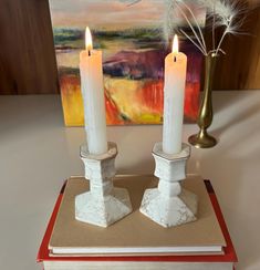 two white candles sitting on top of a book