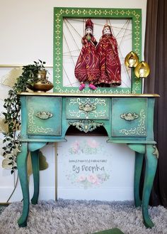 two dolls sitting on top of a green table next to a mirror and potted plant