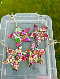 three origami stars are hanging from twine on a plastic container in the grass