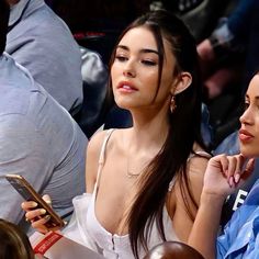 two women sitting next to each other at a basketball game, one looking down and the other holding a cell phone in her hand