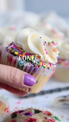 a hand holding a cupcake with white frosting and sprinkles