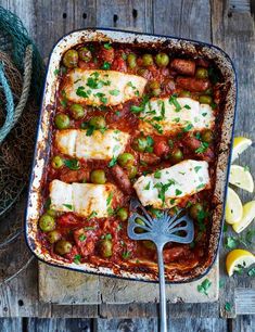 fish in tomato sauce with peas and lemons on a wooden table next to a wire basket