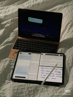 an open laptop computer sitting on top of a bed next to a notebook and pen