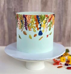 a white cake with colorful leaves on it sitting on a plate next to confetti