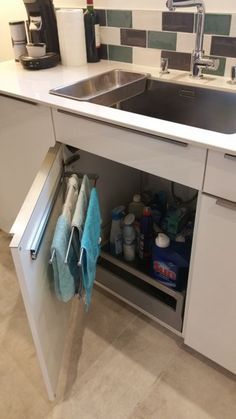 a kitchen sink under a cabinet with towels hanging from it's pull out shelf