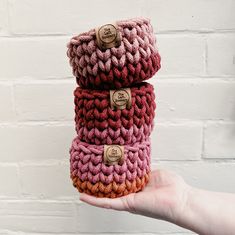 a hand holding three crocheted items in front of a brick wall