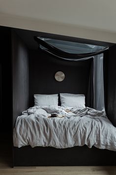 a bed with white linens and pillows in a black walled room, next to a wooden floor