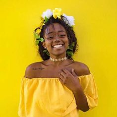 a woman with flowers in her hair smiles while wearing a yellow off the shoulder top