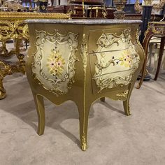 an ornately painted gold cabinet with marble top in a room full of antique furniture