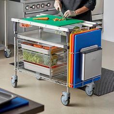 a man cutting up vegetables on top of a kitchen cart with drawers and trays