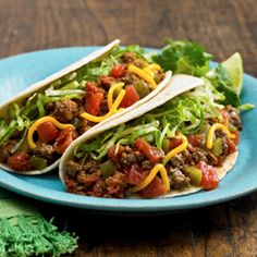 two tacos on a blue plate with lettuce and tomato toppings next to a green napkin