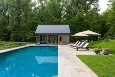 an outdoor pool with lounge chairs and umbrellas next to it in the grass near some trees