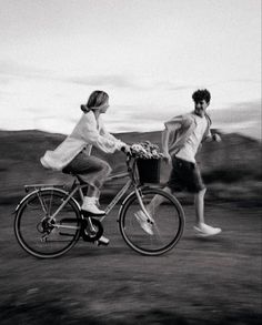 black and white photograph of two people riding bikes on the road with one person holding a basket