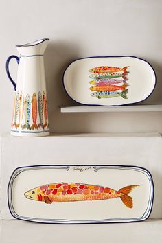 two plates with fish painted on them are next to a pitcher and plate that is shaped like a fish