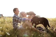 a man and woman are sitting in the grass with their dog, who is looking up into the sky