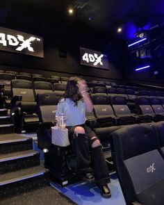 a woman sitting on top of a chair in front of an empty theater seat with the xdx logo above her head