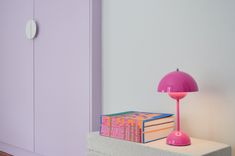 a pink lamp sitting on top of a white shelf next to a stack of books