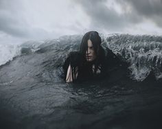 a woman laying on top of a wave in the middle of the ocean with dark clouds above